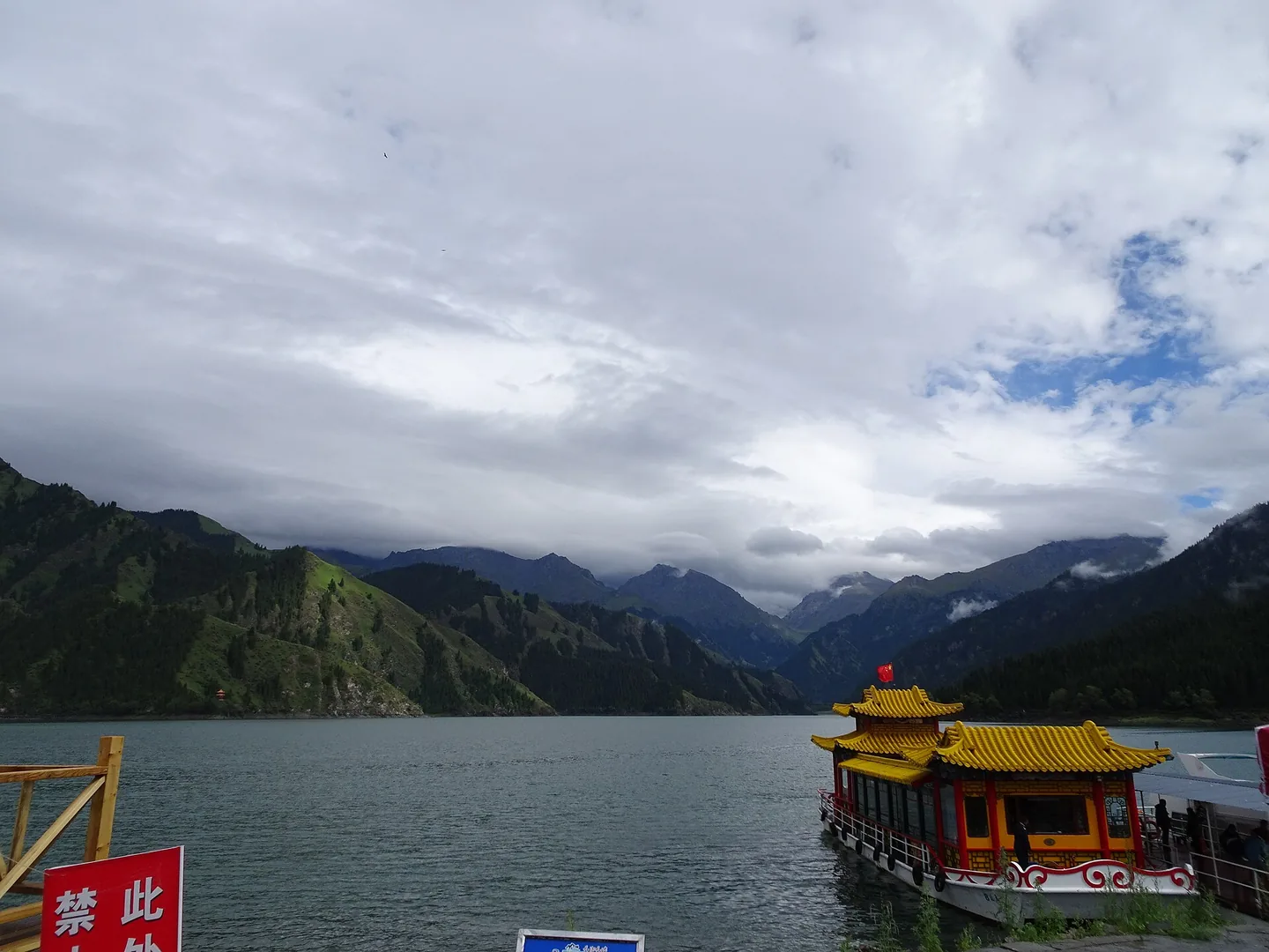 阴云下的天山天池与群山，湖边可见游船码头